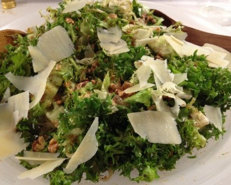 A plate of kale salad with parmesan cheese and walnuts.